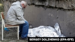 Дедушка сидит рядом с накрытым телом 9-летней внучки возле поликлиники, в которой находится бомбоубежище. Во время ракетного удара оно было закрыто, и люди не смогли туда попасть. Киев, Украина, 1 июня 2023 года